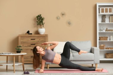 Güzel genç bir kadın oturma odasında yoga yapıyor.