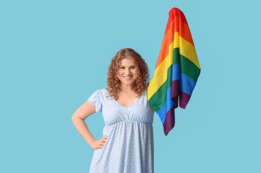 Mavi arka planda LGBT bayrağı olan mutlu genç bir kadın.