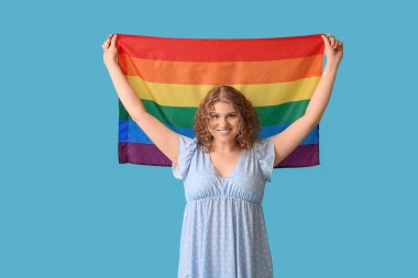 Mavi arka planda LGBT bayrağı olan mutlu genç bir kadın.