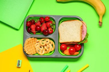 Okul malzemeleri, içinde böğürtlen ve yeşil arka planda sandviç olan beslenme çantası. Üst görünüm