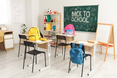 Işık sınıfında okul sıraları, sırt çantaları ve karatahta