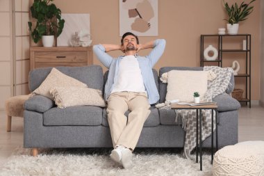 Kanepede dinlenen yakışıklı genç adam. Bej duvarın yanında kliması çalışıyor.