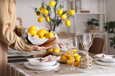 Yemek odasında bir kase taze limonla masa dekorasyonu yapan genç bir kadın.