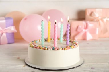 Güzel doğum günü pastası yanan mumlar, hediye kutuları ve balonlar açık ahşap arka planda.