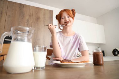 Yüzü lekeli tatlı bir kız. Mutfakta kavanozdan çikolata ezmesi yiyor.