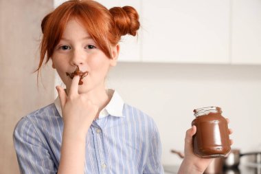 Yüzü lekeli tatlı bir kız. Mutfakta kavanozdan çikolata ezmesi yiyor.