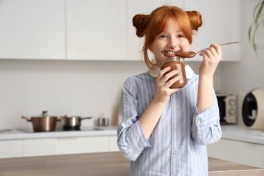 Yüzü lekeli tatlı bir kız. Mutfakta kavanozdan çikolata ezmesi yiyor.