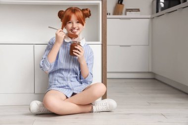 Yüzü lekeli tatlı bir kız. Mutfakta kavanozdan çikolata ezmesi yiyor.