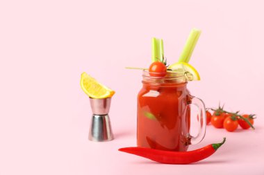 Mason kavanozu içinde kereviz, kırmızı biber ve pembe arka planda limon olan Bloody Mary kokteyli.