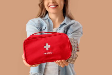 İlk yardım çantası ve bej arka planda hapları olan güzel bir genç kadın. Yakın plan.