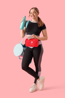 Pembe arka planda ilk yardım çantası ve su şişesi olan genç bir kadın.