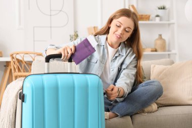 Oturma odasındaki kanepede bavulu ve pasaportu olan güzel genç bir kadın oturuyor. Seyahat kavramı