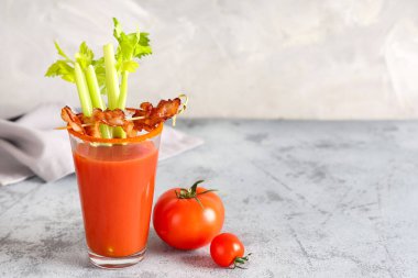 Bir bardak Bloody Mary kokteyli, domuz pastırması ve gri arka planda kereviz.