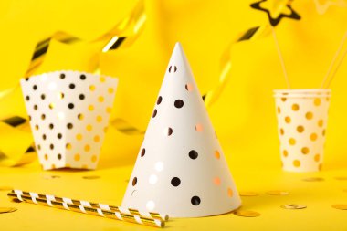 Parti şapkası, karton bardaklar, sarı arka planda kutu ve konfeti.