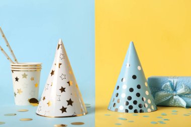 Renkli arka planda parti şapkaları, fincanları, pipetleri ve hediye kutusuyla kompozisyon