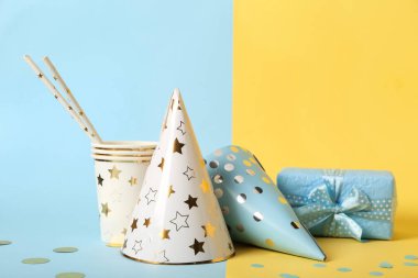 Renkli arka planda parti şapkaları, fincanları, pipetleri ve hediye kutusuyla kompozisyon