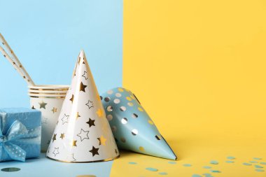 Renkli arka planda parti şapkaları, fincanları, pipetleri ve hediye kutusuyla kompozisyon