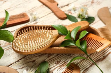 Hafif ahşap arka planda saç fırçası, tarak ve bitki dallarıyla kompozisyon