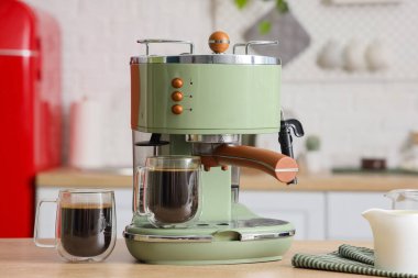 Mutfaktaki masada kahve fincanı ve süt olan modern kahve makinesi.