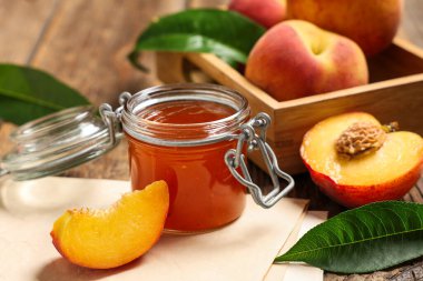 Kavanoz dolusu tatlı şeftali reçeli, taze meyve ve tahta masa üzerinde kağıt çarşaf.