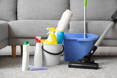 Kova dolusu temizlik malzemesi, paspas ve süpürge oturma odasındaki halının üstünde.