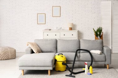 Salondaki halının üzerinde temizlik malzemeleri ve modern elektrikli süpürge var.
