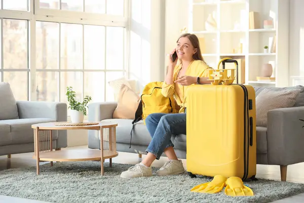 Çantalı, kulaklıklı ve çantalı güzel bir kadın oturma odasında telefonla konuşuyor. Seyahat kavramı