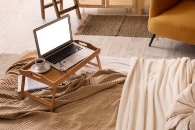 Modern dizüstü bilgisayarlı ahşap bir masa ve şık bir yatak odasında rahat bir yatakta bir fincan kahve.