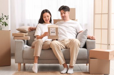 Genç çift evdeki kanepede paket kutusunu açıyor.