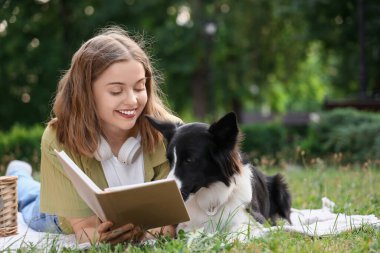 Parkta piknik üzerine kitap okuyan sevimli bir Collie köpeği olan güzel genç kadın.