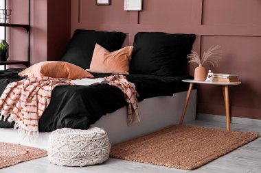 Modern yatak odası, rahat yatak odası, siyah çarşaflar ve kahverengi duvarın yanındaki komodin.