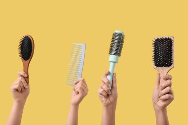 Sarı arka planda farklı kuaför fırçaları olan kadın elleri.