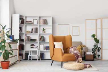 Kahverengi koltuklu, hasır puflu ve kitaplıklı şık bir oturma odası.