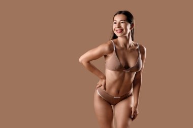 Kahverengi arka planda selülit sorunu olan iç çamaşırlı genç bir kadın.