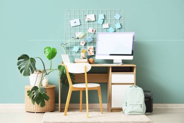 Modern bilgisayar, sırt çantası ve mavi duvarın yanındaki ruh hali panosuyla rahat çalışma alanı