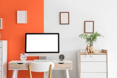 Modern bilgisayar, alarm saatleri ve renk duvarına yakın ev bitkileriyle rahat çalışma alanı