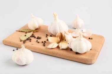 Taze sarımsaklı ahşap tahta, karabiber ve gri arka planda körfez yaprakları.