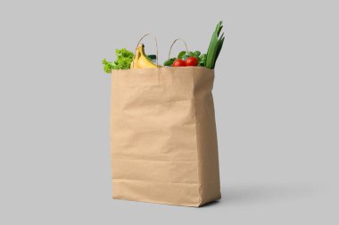 Gri arka planda farklı bakkaliye malzemeleriyle dolu kağıt torba.