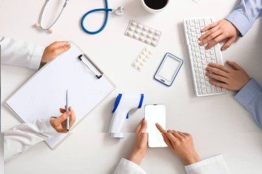 Klavyesi, cep telefonu ve panosu olan doktorlar beyaz masada çalışıyor, üst görünüm