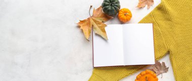 Açık bir kitap, kıyafetler ve arka planda sonbahar dekoru olan kompozisyon