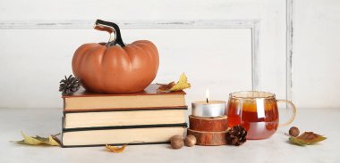 Dekoratif balkabağı, sonbahar yaprakları, kitaplar ve çay fincanı ışık duvarının yanındaki masada.