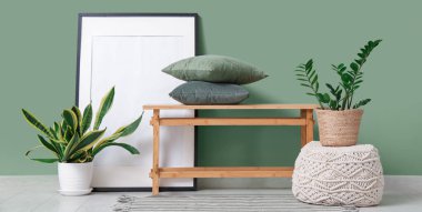 Odadaki yeşil duvarın yanında, çiçekli, yastıklı ve çerçeveli bir bank.