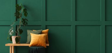 Dekoratif yastıklı ahşap bank, palmiye ağacı ve oda yeşil duvarın yanında puf.