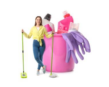 Beyaz arka planda yer paspası ve büyük bir kova temizlik malzemesi olan genç bir kadın.