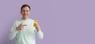 Mor arka planda balık yağı kapsülleri tutan genç bir adam.