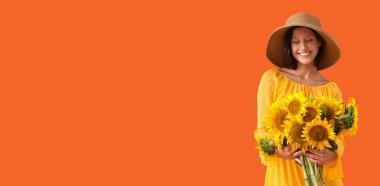 Turuncu arka planda bir buket ayçiçeği tutan genç ve güzel bir kadın.