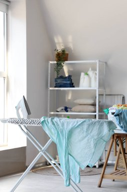 Çamaşır odasındaki ütü masasında elektrikli ütü ve buruşuk gömlek.