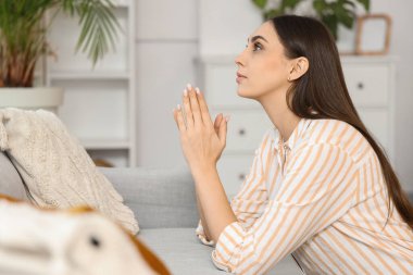 Evdeki kanepenin yanında dua eden güzel bir kadın.