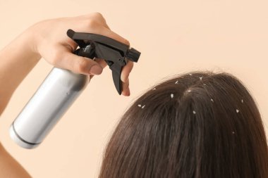 Kepek sorunu olan genç bir kadın. Bej arka plana saç spreyi sıkıyor. Yakın plan.