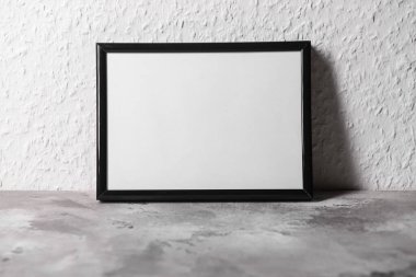 Beyaz duvarın yanındaki gri masada güzel boş fotoğraf çerçevesi.